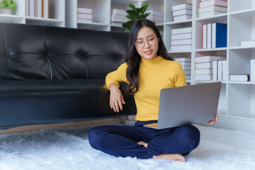 Cute Asian young woman using laptop computer in the living room, watching movie, listening to music, shopping online, watching live broadcast.