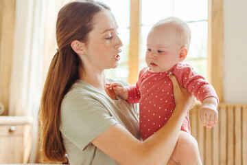 Wall Mural - Beautiful young mother holding her little baby comforting her in living room at home