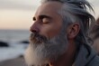 © Ina725 - Close up of handsome medium-aged meditating man with gray hair and beard on the ocean shore, with closed eyes