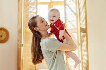 Wall Mural - Mother holding her cute little baby in living room at home. Babysitter taking care of infant