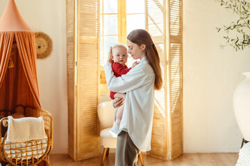 Wall Mural - Beautiful young mother with closed eyes holding little baby in living room at home