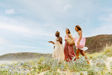 three friends walk happily together to the beach. multiracial group of women enjoying summer vacation on the coast.