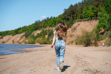 A teenage girl with long hair and jeans runs and frolics on the beach