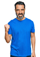 Sticker - Middle aged man with beard wearing casual blue t shirt angry and mad raising fist frustrated and furious while shouting with anger. rage and aggressive concept.