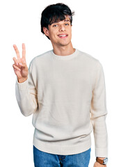 Sticker - Handsome hipster young man wearing casual winter sweater showing and pointing up with fingers number two while smiling confident and happy.