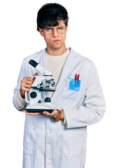 Canvas Print - Handsome hipster young man wearing lab coat holding microscope skeptic and nervous, frowning upset because of problem. negative person.