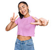 © Krakenimages.com - Hispanic teenager girl with dental braces wearing casual clothes smiling with tongue out showing fingers of both hands doing victory sign. number two.