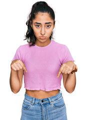 Wall Mural - Hispanic teenager girl with dental braces wearing casual clothes pointing down looking sad and upset, indicating direction with fingers, unhappy and depressed.