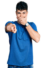 Sticker - Young hispanic man wearing casual t shirt laughing at you, pointing finger to the camera with hand over mouth, shame expression