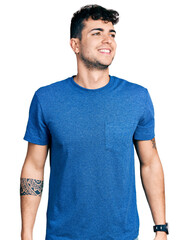 Poster - Young hispanic man wearing casual t shirt looking away to side with smile on face, natural expression. laughing confident.