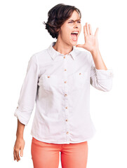 Wall Mural - Beautiful young woman with short hair wearing elegant white shirt shouting and screaming loud to side with hand on mouth. communication concept.