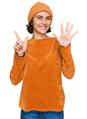 Sticker - Young hispanic woman wearing casual clothes and wool cap showing and pointing up with fingers number seven while smiling confident and happy.