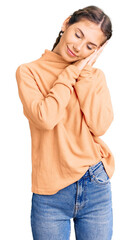 Beautiful caucasian woman with blonde hair wearing casual winter sweater sleeping tired dreaming and posing with hands together while smiling with closed eyes.