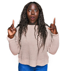 Poster - Young african woman wearing wool winter sweater amazed and surprised looking up and pointing with fingers and raised arms.