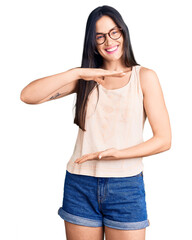 Sticker - Young beautiful caucasian woman wearing casual clothes and glasses gesturing with hands showing big and large size sign, measure symbol. smiling looking at the camera. measuring concept.