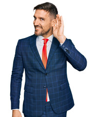 Canvas Print - Handsome man with beard wearing business suit and tie smiling with hand over ear listening an hearing to rumor or gossip. deafness concept.