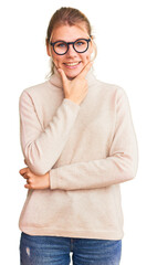 Wall Mural - Young beautiful blonde woman wearing turtleneck sweater and glasses looking confident at the camera smiling with crossed arms and hand raised on chin. thinking positive.