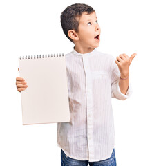 Poster - Cute blond kid holding notebook pointing thumb up to the side smiling happy with open mouth