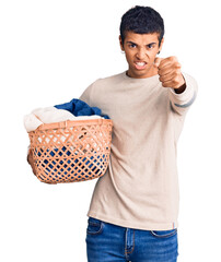 Wall Mural - Young african amercian man holding laundry basket annoyed and frustrated shouting with anger, yelling crazy with anger and hand raised