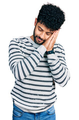 Poster - Young arab man with beard wearing casual striped sweater sleeping tired dreaming and posing with hands together while smiling with closed eyes.