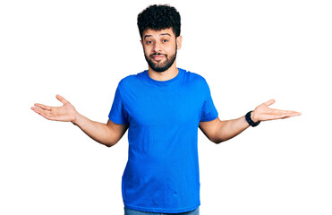 Poster - Young arab man with beard wearing casual blue t shirt clueless and confused expression with arms and hands raised. doubt concept.