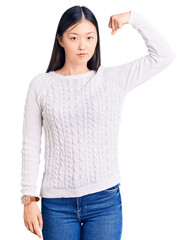 Wall Mural - Young beautiful chinese woman wearing casual sweater strong person showing arm muscle, confident and proud of power