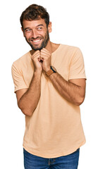 Canvas Print - Handsome young man with beard wearing casual tshirt laughing nervous and excited with hands on chin looking to the side