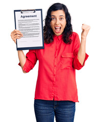 Poster - Young beautiful hispanic woman holding clipboard with agreement document screaming proud, celebrating victory and success very excited with raised arms