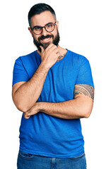 Wall Mural - Hispanic man with beard wearing casual t shirt and glasses looking confident at the camera smiling with crossed arms and hand raised on chin. thinking positive.