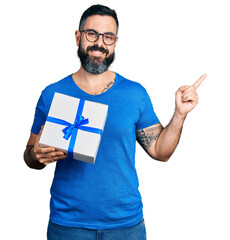 Wall Mural - Hispanic man with beard holding gift smiling happy pointing with hand and finger to the side