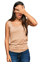 Sticker - Beautiful hispanic woman wearing casual clothes peeking in shock covering face and eyes with hand, looking through fingers with embarrassed expression.