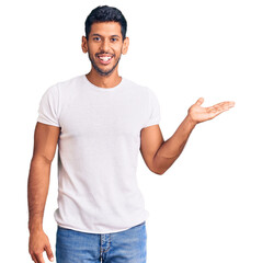 Sticker - Young latin man wearing casual clothes smiling cheerful presenting and pointing with palm of hand looking at the camera.