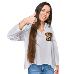 Wall Mural - Young hispanic girl wearing casual clothes doing happy thumbs up gesture with hand. approving expression looking at the camera showing success.