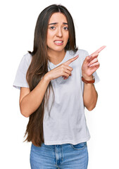 Sticker - Young hispanic girl wearing casual white t shirt pointing aside worried and nervous with both hands, concerned and surprised expression