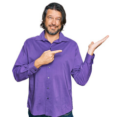 Canvas Print - Middle age handsome man wearing business shirt amazed and smiling to the camera while presenting with hand and pointing with finger.