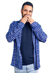 Poster - Young hispanic man wearing casual clothes laughing and embarrassed giggle covering mouth with hands, gossip and scandal concept