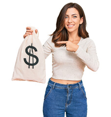 Canvas Print - Young brunette woman holding dollars bag smiling happy pointing with hand and finger