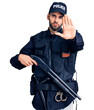© Krakenimages.com - Young handsome man with beard wearing police uniform holding shotgun with open hand doing stop sign with serious and confident expression, defense gesture