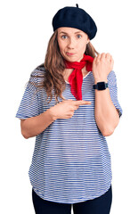 Poster - Young beautiful blonde woman wearing french beret and striped t-shirt in hurry pointing to watch time, impatience, looking at the camera with relaxed expression