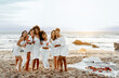 © Prostock-studio - Smiling young ladies with glasses of wine embracing posing standing on the beach, celebrating bachelorette party