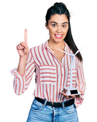 Poster - Young hispanic woman holding solar windmill for renewable electricity smiling with an idea or question pointing finger with happy face, number one