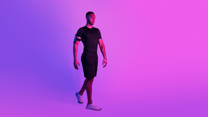 Wall Mural - Sporty African Man With Phone Armband Walking On Purple Background