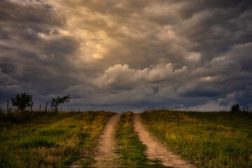 Wall Mural - deserted country dirt road up over hilltop under evening dramatic cloudy sky