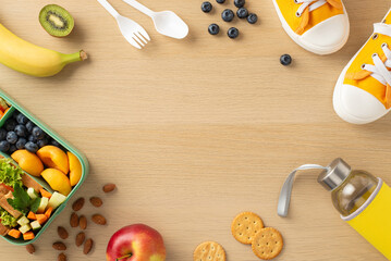 Promoting healthy eating in schools. Top view of lunchbox filled with nutritious items: fruits, vegetables, sandwich, berries, nuts, cookies, bottle, sneakers on wooden desk with space for text or ad