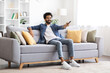 © Prostock-studio - Portrait Of Happy Young Indian Guy Watching TV On Couch At Home