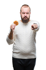 Wall Mural - Young caucasian hipster man eating sweet waffle over isolated background pointing with finger to the camera and to you, hand sign, positive and confident gesture from the front