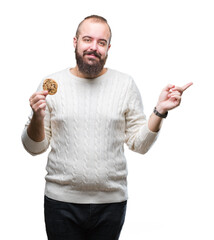 Sticker - Young hipster man eating chocolate chips cookie over isolated background very happy pointing with hand and finger to the side