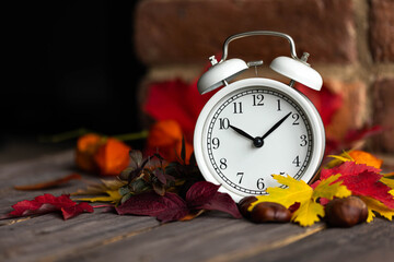 Wall Mural - Fall winter time change concept. Autumn composition with retro alarm clock, bright yellow and red leaves, walnut. Brick wall on background. Cozy home atmosphere. Close-up