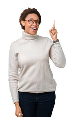 Sticker - Young beautiful african american woman wearing glasses over isolated background pointing finger up with successful idea. Exited and happy. Number one.