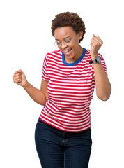 Sticker - Beautiful young african american woman wearing glasses over isolated background very happy and excited doing winner gesture with arms raised, smiling and screaming for success. Celebration concept.